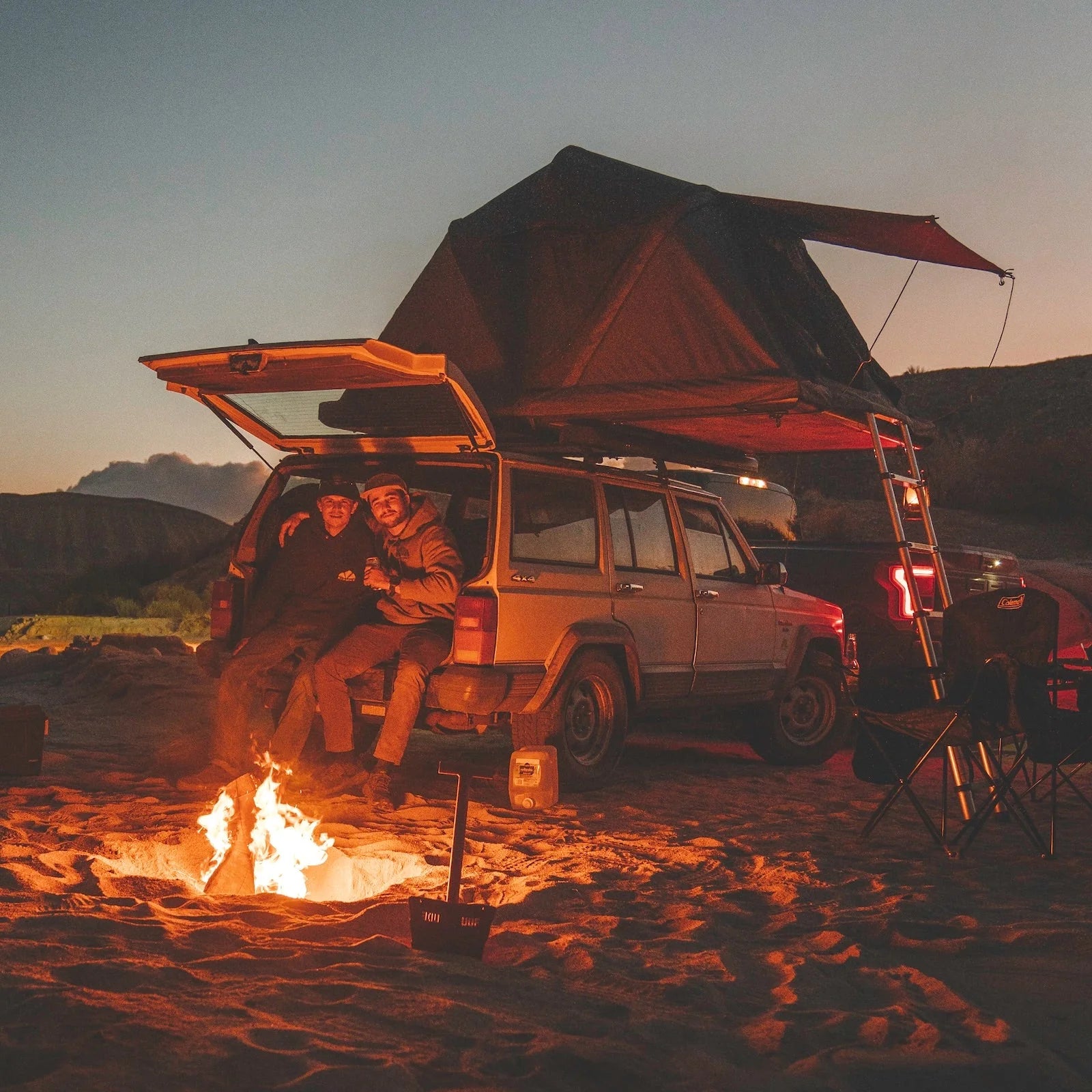 Deux amis devant un feu de camp, leur tente de toit Roof Space est installée sur leur 4x4