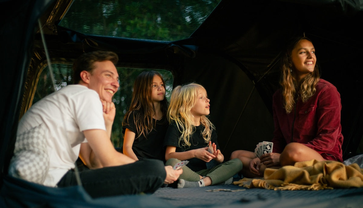 Une famille assise dans une tente de toit pour 4 personnes avec le mode panoramique ouvert.